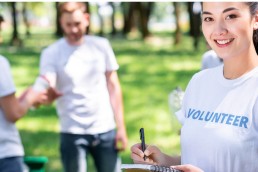girl writing in textbook while volunteers cleaning park