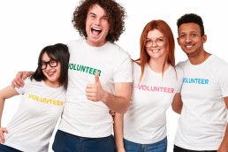 group of 4 individuals wearing volunteer t-shirts smiling at the camera