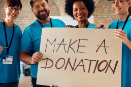 4 volunteers inviting people to donate to charity while holding a placard saying Make a donation