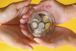 four hands coming together and holding a glass jar of coins