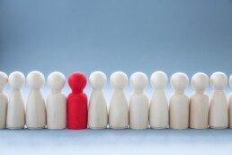 a selection of plain wooded figures in a line with one red one standing out.